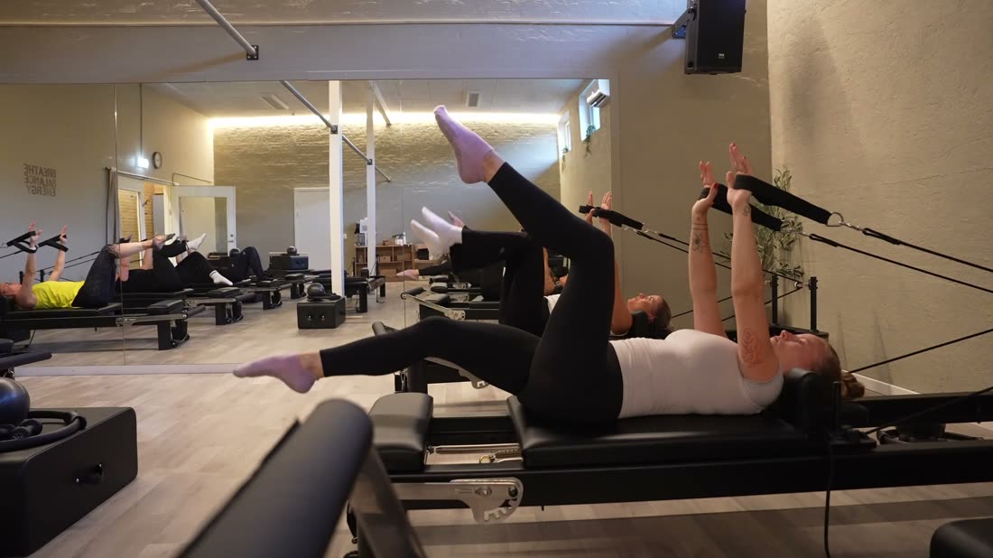 Reformer-hold træner liggende med benene i remmene
